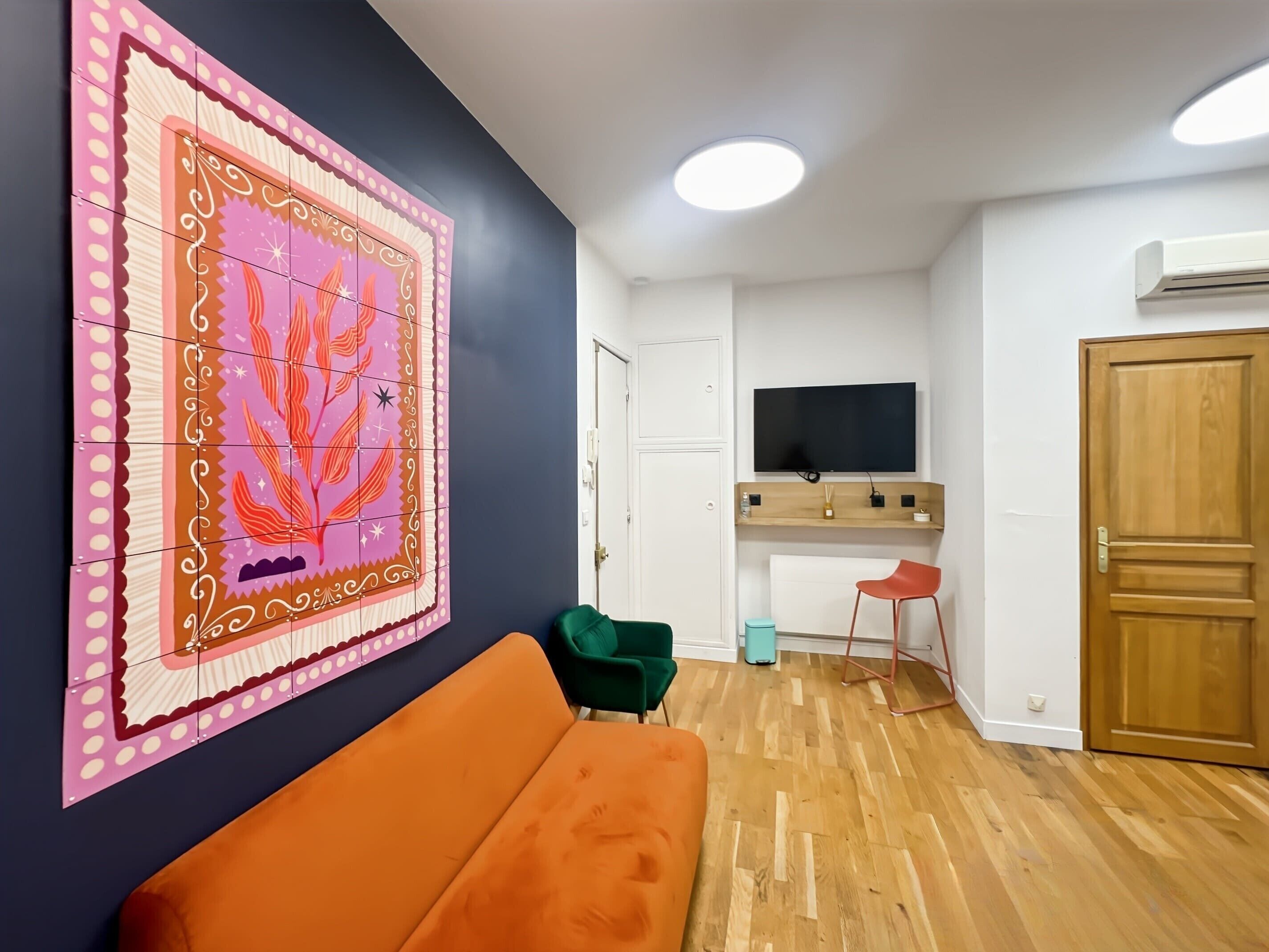 A room with a wooden floor, a sofa, a TV mounted on the wall, a door, and a wall-mounted air conditioner.