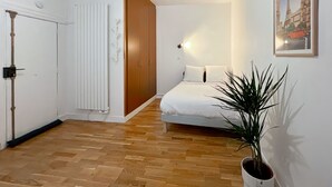 A bedroom with a bed, a radiator, a wardrobe, and a potted plant.