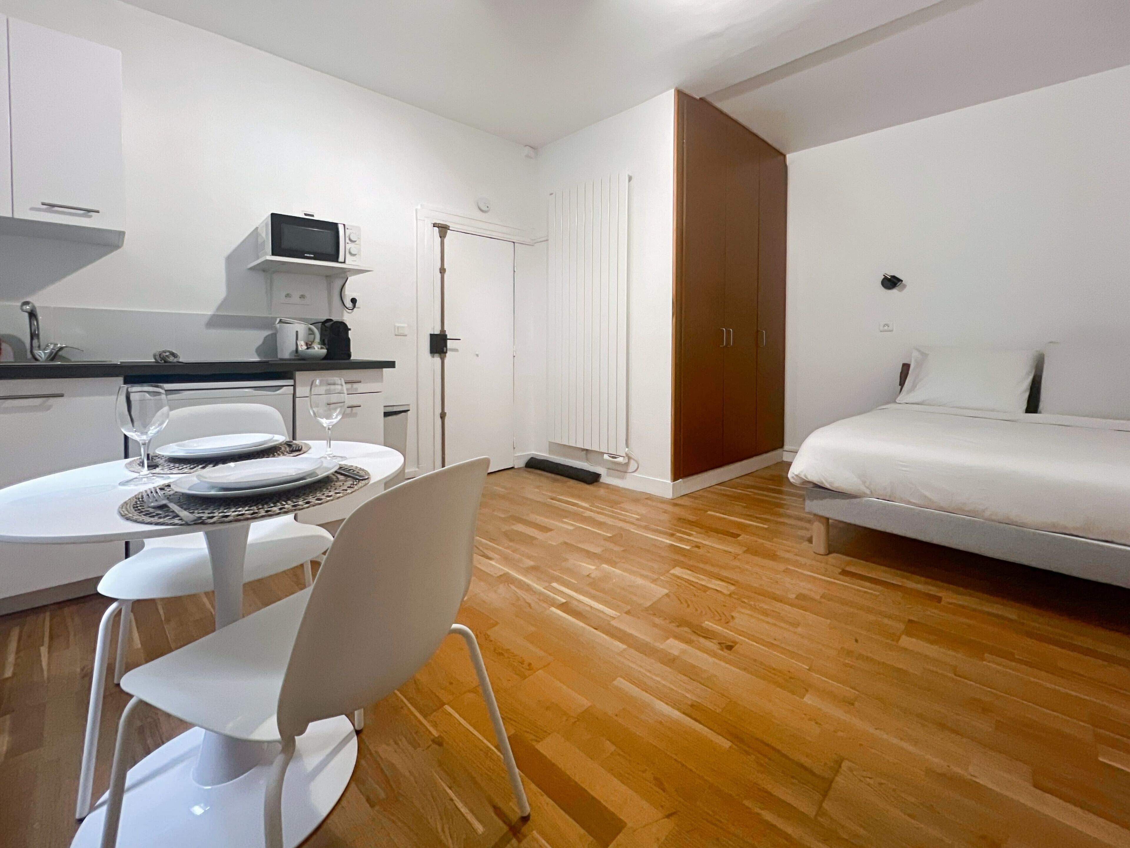 Une pièce compacte comprenant un coin cuisine, un espace repas avec une table et des chaises, et un lit.