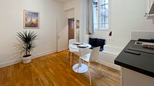 A modern kitchen with white cabinets, a black countertop, and a dining area with white chairs and a table.