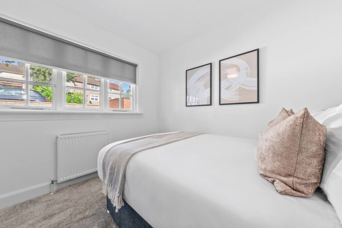 A bedroom with a bed, a window with a view of buildings, and two framed pictures on the wall.