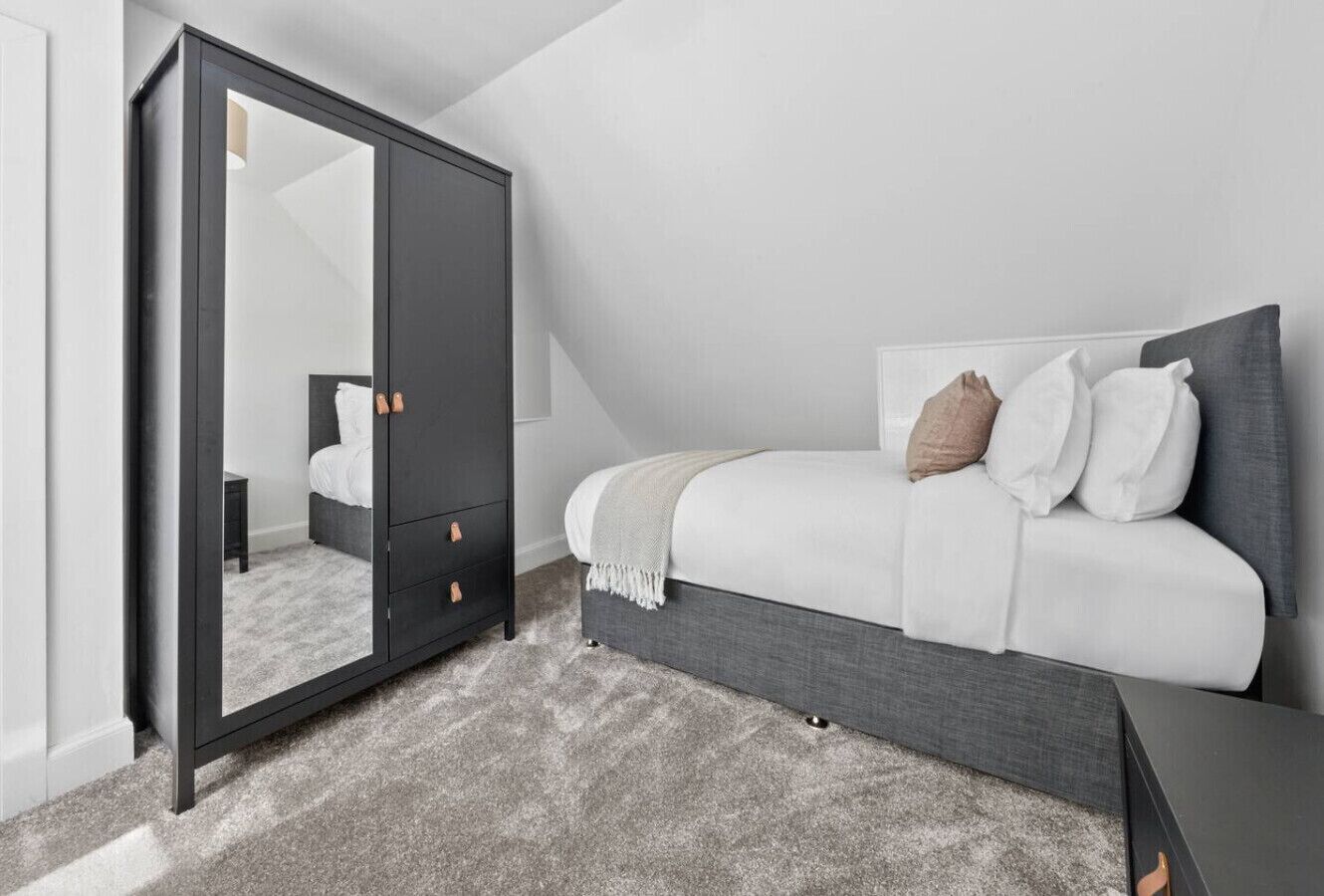 Une chambre à coucher avec un lit, une armoire sombre, une petite table de chevet et un sol recouvert d’une moquette.