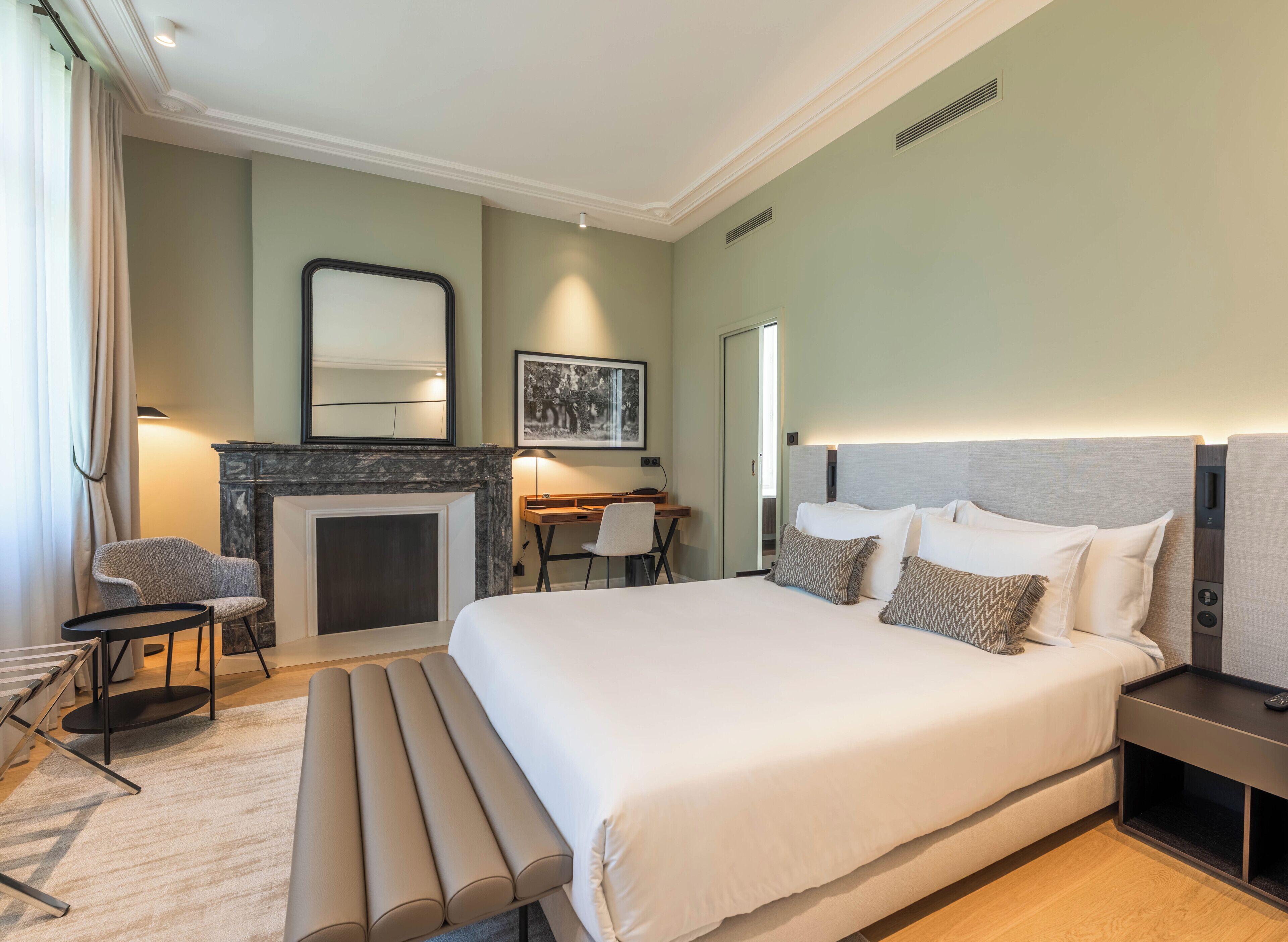 Una habitación de hotel moderna con una cama grande, un escritorio, una silla, una chimenea y un espejo amplio.