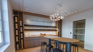 A modern interior with a wooden bar area, a large table with stools, and a unique ceiling light fixture. - La Villa des Vignes (Saint-Émilion)