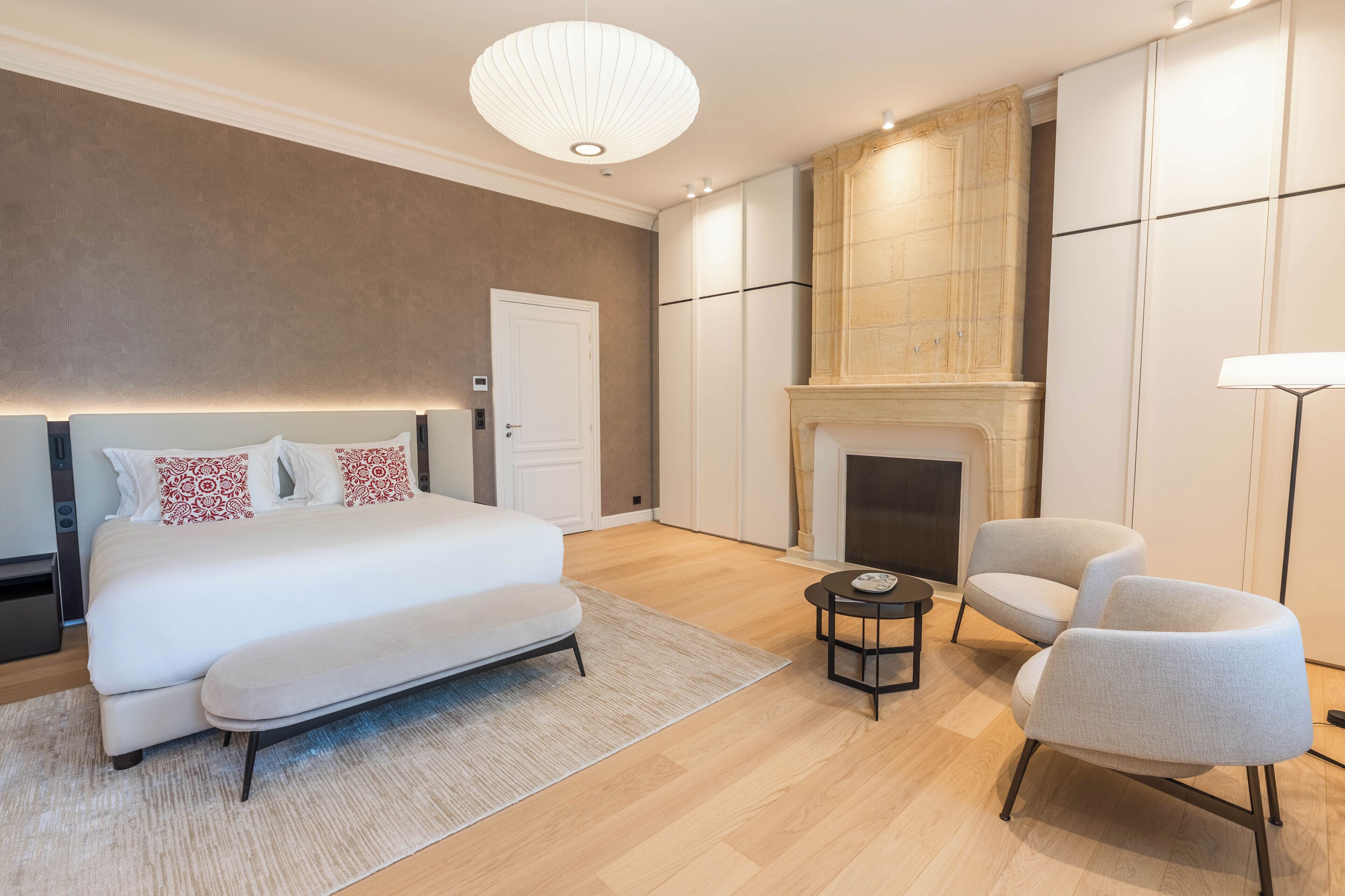 A modern bedroom with a large bed, a fireplace, a seating area, and a ceiling light fixture.