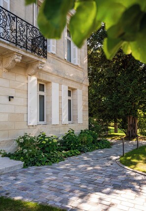 A stone building with white shutters, a paved pathway, and lush greenery. - La Villa des Vignes (Saint-Émilion)