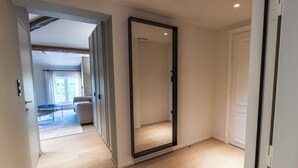 Un pasillo con un espejo grande, una puerta y vista a otra habitación con una mesa y un sofá.