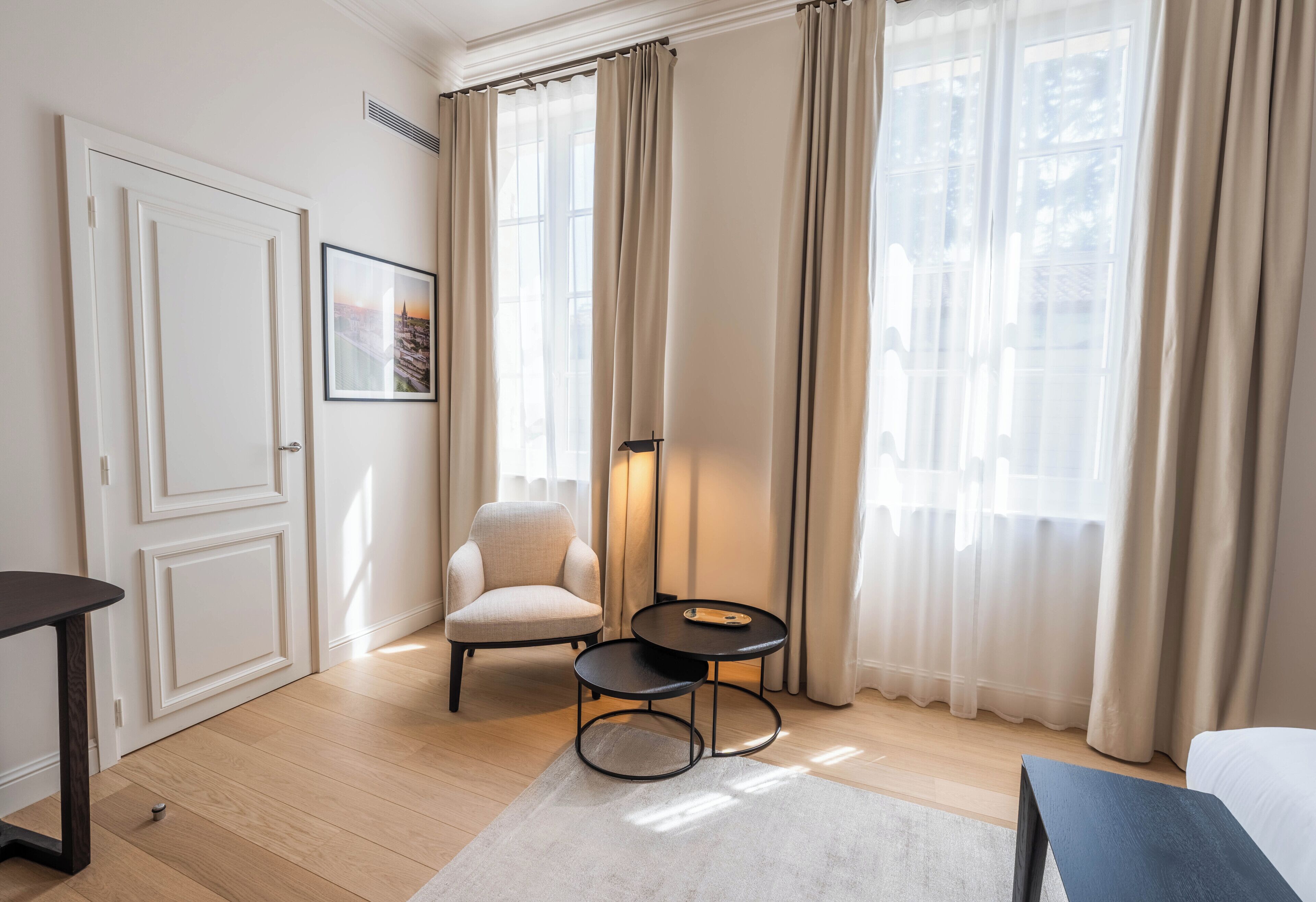 A hotel room with a bed, a chair, a small table, and a picture on the wall.