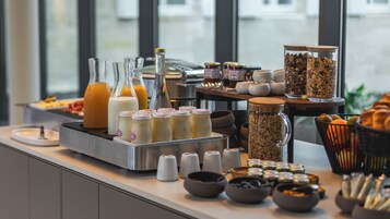 Un bufé de desayuno con diversas opciones de comida y bebidas, como jugos, leche, cereales y pasteles.