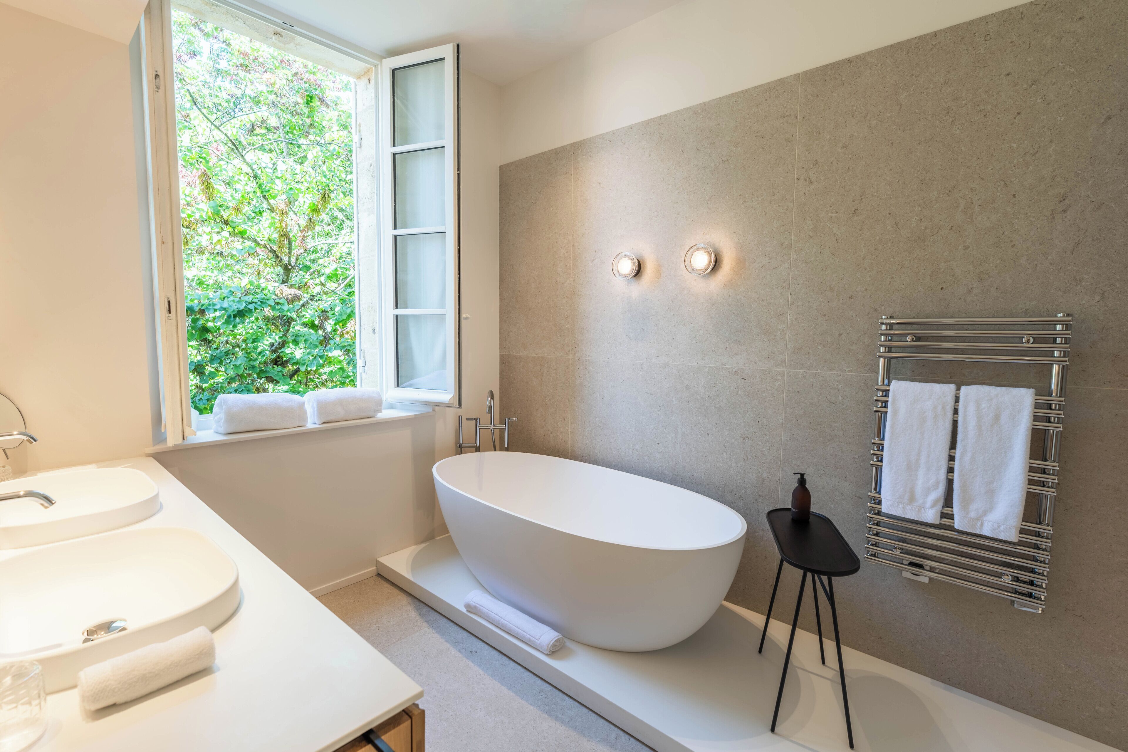 A modern bathroom with a freestanding bathtub, a double sink, and a towel rack with towels.