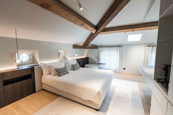 Un dormitorio con una cama grande, vigas de madera, una mesita de noche con lámpara y vistas al exterior.