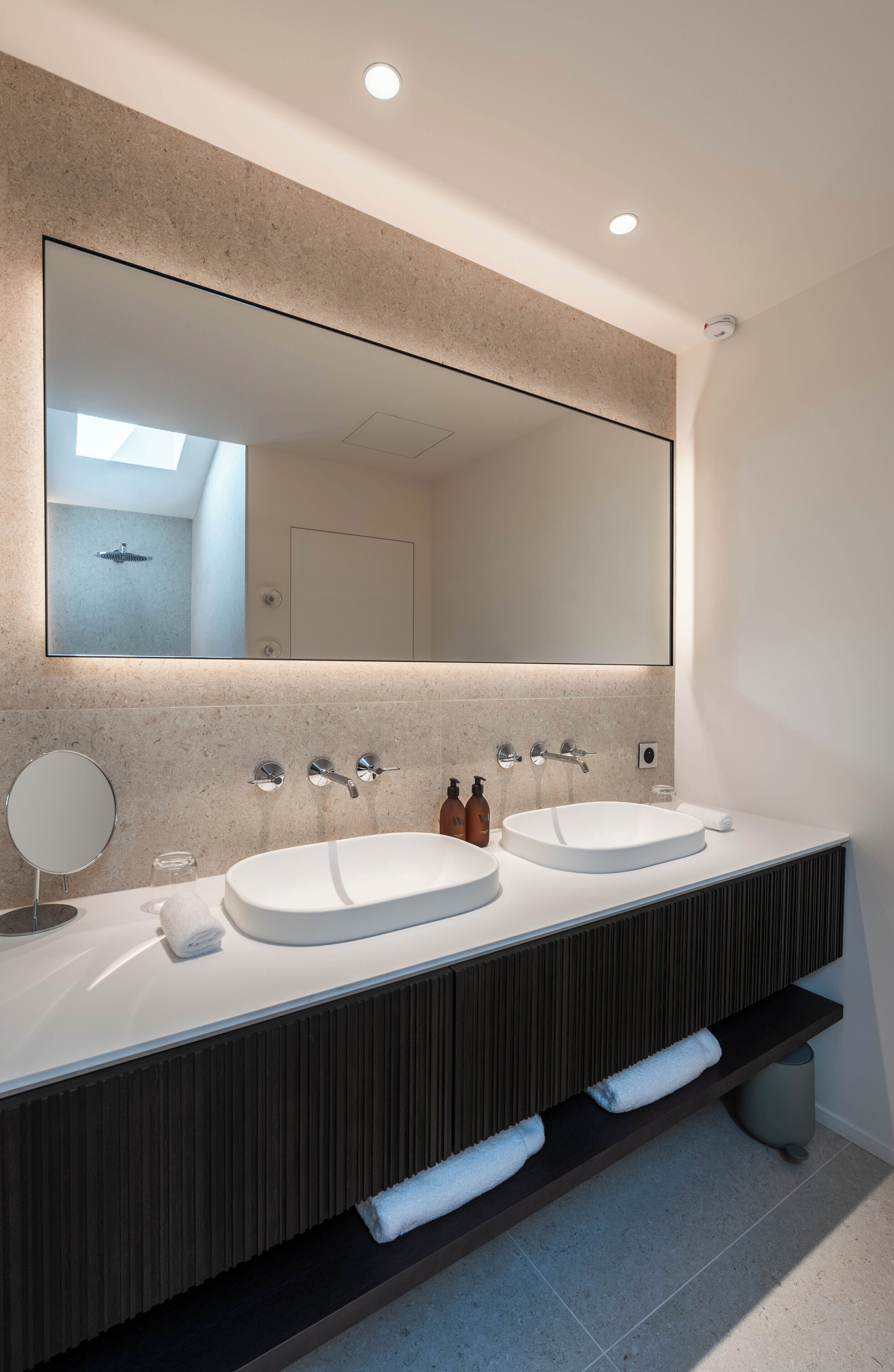 A modern bathroom with two sinks, a large mirror, and a towel rack.