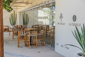 A restaurant interior with wooden tables and chairs, a glass wall with cacti, and a sign reading 'MAJAGUA LA CIRCUELA'.