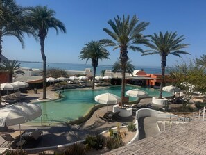 A pool area with lounge chairs, umbrellas, and palm trees.