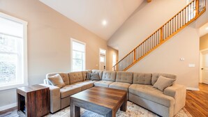 A spacious living room with a large sectional sofa, a wooden coffee table, and a staircase. - NF72: Brand New, Creekside home, 3 King Suites, Hot Tub. Firepit (Davis)
