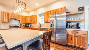 A modern kitchen with wooden cabinets, a stainless steel refrigerator, and a large island with seating. - NF72: Brand New, Creekside home, 3 King Suites, Hot Tub. Firepit (Davis)