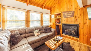 A cozy living room with a wooden ceiling, a leather sofa, a fireplace, and a sign indicating it's in Monongahela National Forest. - Cozy Updated Cabin, close to towns, A/C (Davis)