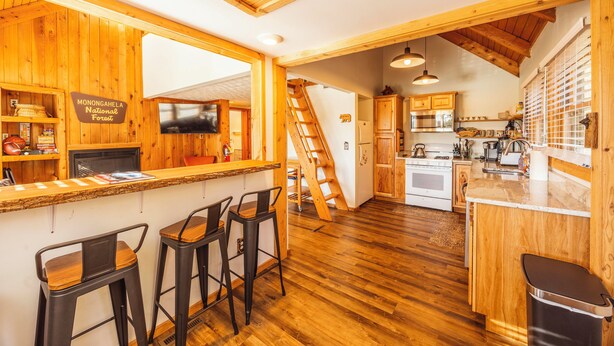 A kitchen with wooden cabinets, a bar area with stools, a television, and a sign indicating the location is Monongahela National Forest. - Cozy Updated Cabin, close to towns, A/C (Davis)