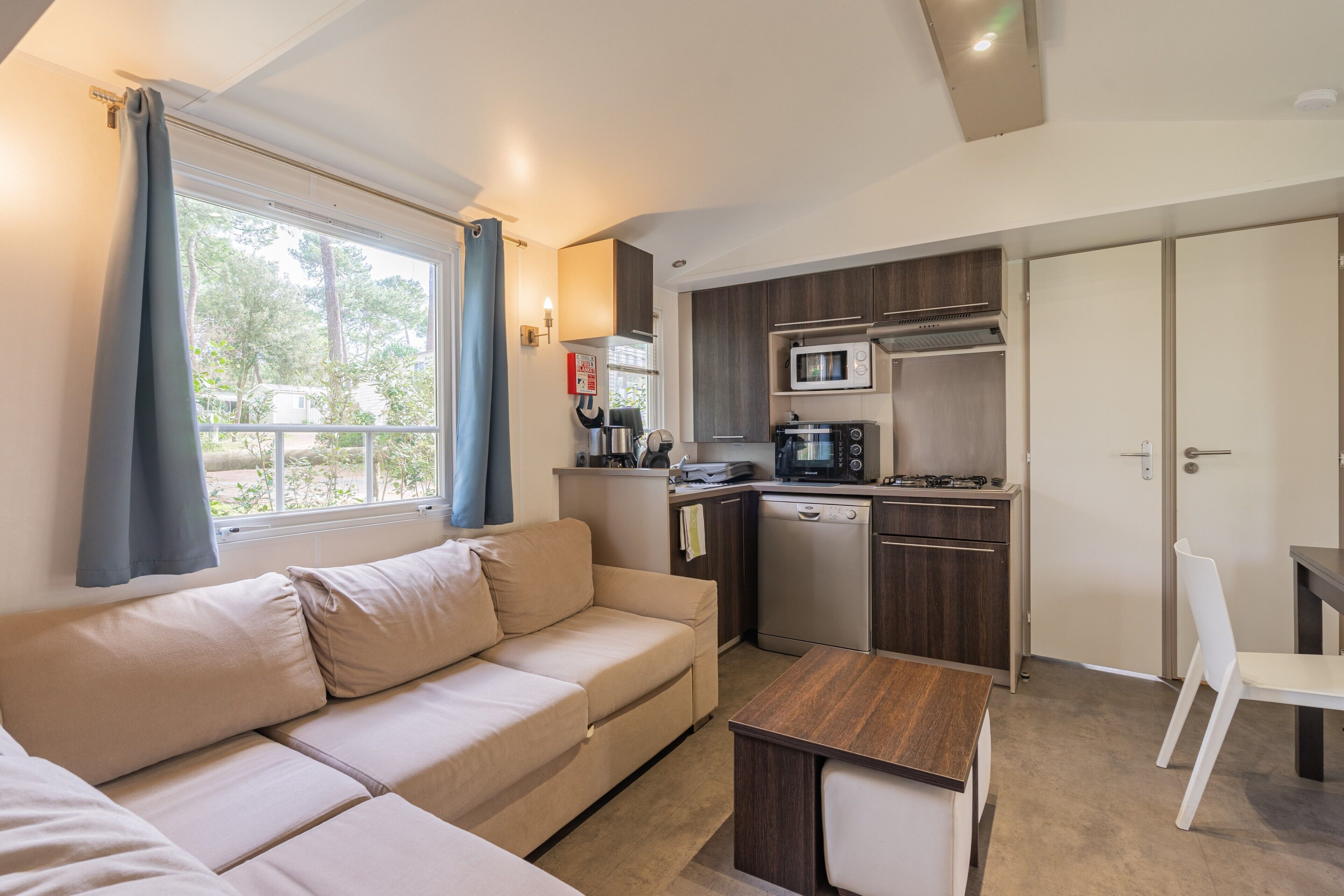 Un espace de vie compact comprenant un canapé, une table à manger, un coin cuisine avec un four à micro-ondes et une cuisinière, et une vue par la fenêtre.