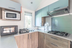 A kitchen with a microwave, toaster oven, stove, and wooden cabinets. - Mobile Home on Oléron in 5-Star Campsite with Shared Pool (Saint George d'Oleron)