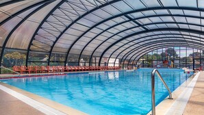 A large indoor swimming pool with a curved glass roof, red chairs along the poolside, and a lifeguard stand. - Mobile Home on Oléron in 5-Star Campsite with Shared Pool (Saint George d'Oleron)