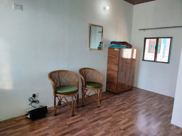 Una habitación con dos sillas de mimbre, un armario de madera, un espejo y una ventana con vistas a edificios.