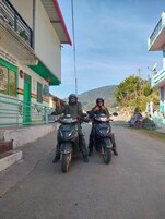 Two individuals on motorcycles parked in front of a building with a green door and a satellite dish.