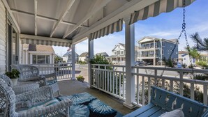 A covered porch with wicker furniture and a swing, overlooking a residential street with houses. - Hot Tub| 3BR Lavallette| Girls Trip at the Beach (Lavallette)