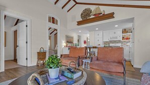 A spacious living room with a dark wooden coffee table, a sofa, and a dining area with white cabinets and a kitchen in the background. - Hot Tub| 3BR Lavallette| Girls Trip at the Beach (Lavallette)