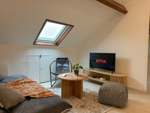 Un salon chaleureux avec une lucarne, un téléviseur, un canapé confortable, une petite table ronde et un pouf à motifs.