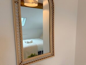 Un miroir doté d’un cadre ajouré qui reflète un lit avec des oreillers et une petite plante.