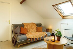 Ein gemütliches Schlafzimmer im Loft-Stil mit schrägem Dach, einer Schlafsofa, einem kleinen runden Tisch, einer Topfpflanze und einem Nachttisch mit Kerze.