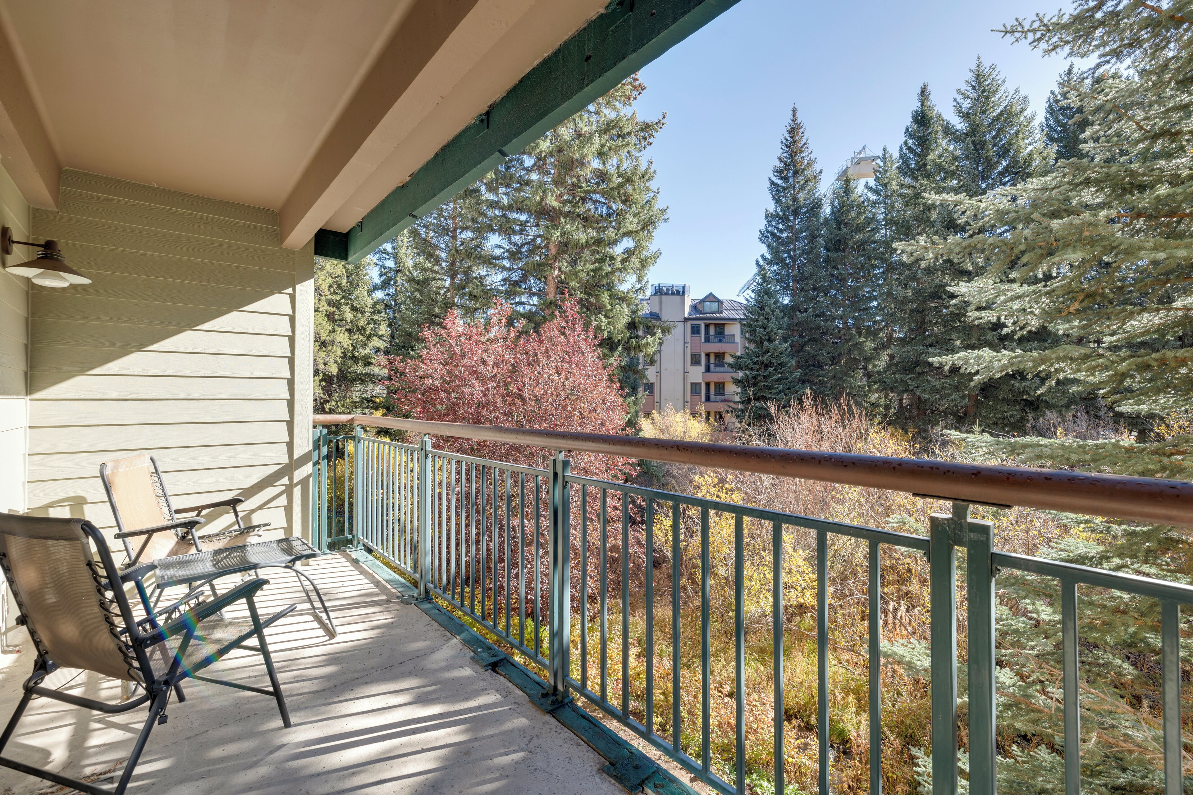 Un balcon aménagé avec du mobilier d’extérieur, offrant une vue sur les arbres et les bâtiments.