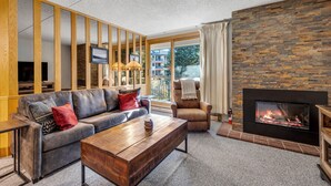 Ein modernes Wohnzimmer mit einer Ledersofa, einem Holztisch, einem Kamin und einem großen Fenster mit Blick ins Freie.