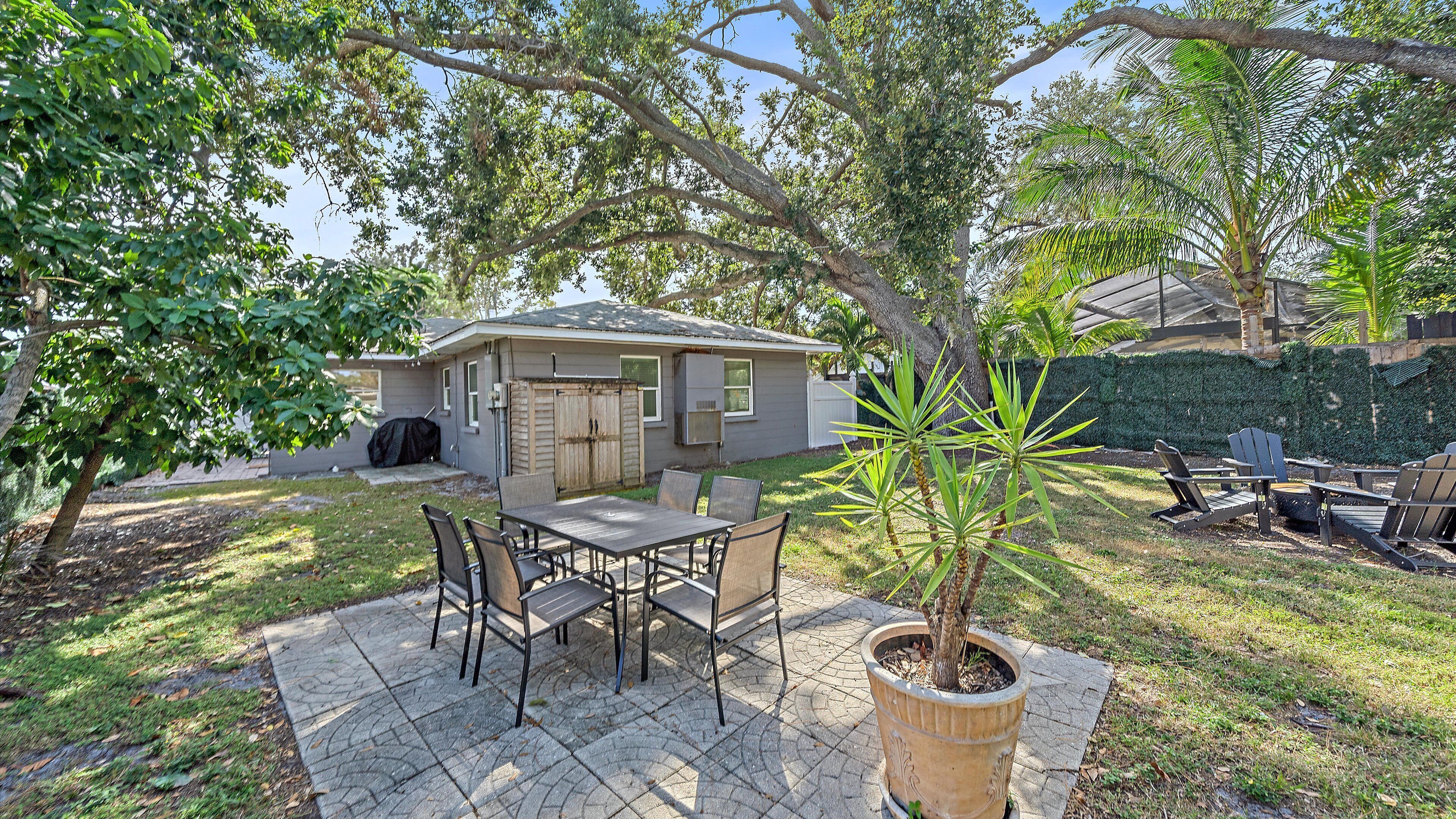 Une terrasse avec une table et des chaises, un pot de fleurs et une maison en arrière-plan.