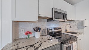 A modern kitchen with white cabinets, a stainless steel microwave, an oven, and a granite countertop.