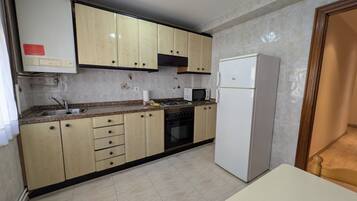 Une cuisine avec des meubles de couleur beige, un réfrigérateur blanc, un four à micro-ondes et une cuisinière.
