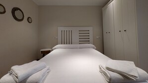 Un lit bien fait, avec du linge de lit et des serviettes blanches, une table de chevet et une armoire à plusieurs portes.
