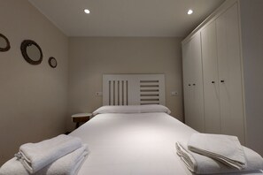 Un letto rifatto con lenzuola e asciugamani bianchi, un comodino e un armadio con ante multiple.
