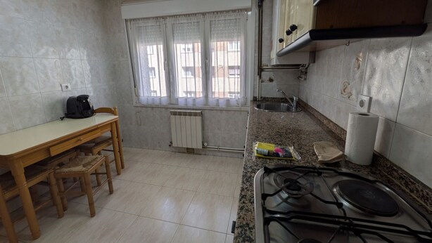Une cuisine équipée d’une cuisinière à gaz, d’une fenêtre avec des rideaux, d’un radiateur et d’une table à manger avec des chaises.