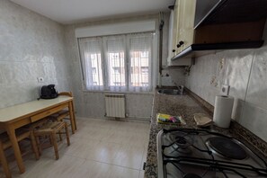 Une cuisine équipée d’une cuisinière à gaz, d’une fenêtre avec des rideaux, d’un radiateur et d’une table à manger avec des chaises.