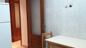 Une cuisine avec un réfrigérateur blanc, une porte en bois et une table avec une chaise.
