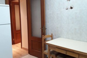Una cucina con frigorifero bianco, porta in legno e tavolo con una sedia.