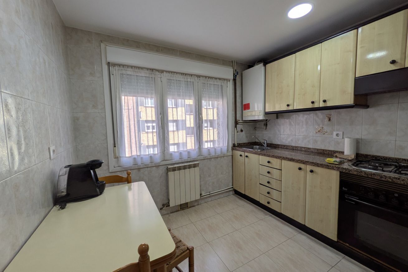 Una cuina amb taula de menjador, armaris, fogó i finestra amb cortines.