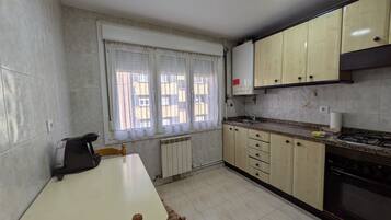 Una cuina amb taula de menjador, armaris, fogó i finestra amb cortines.