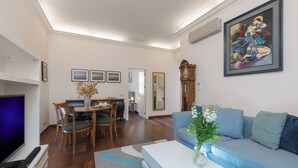 A modern living room with a sofa, coffee table, TV, dining area, and artwork on the wall.