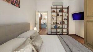 A hotel room with a large bed, a bookshelf, a television, and a door leading to another room.