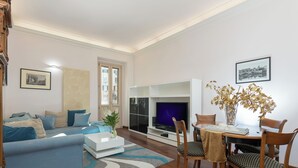 A living room with a sofa, TV, and dining area with chairs and a table.