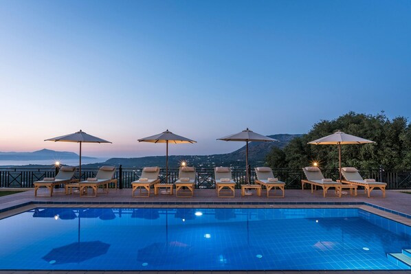 A poolside area with lounge chairs and umbrellas, overlooking a mountainous landscape. - Erato Villa in Gavalochori (Apokoronas)
