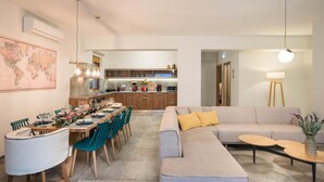 Ein modernes Wohnzimmer mit einem grauen Sofa, türkisfarbenen Sesseln und einem Essbereich mit einem Holztisch, gedeckt für sechs Personen.